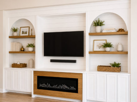 Custom media wall featuring white built-in cabinetry, arched display shelves with white oak accents, a mounted television, shiplap backing, and a linear electric fireplace with a white oak surround.