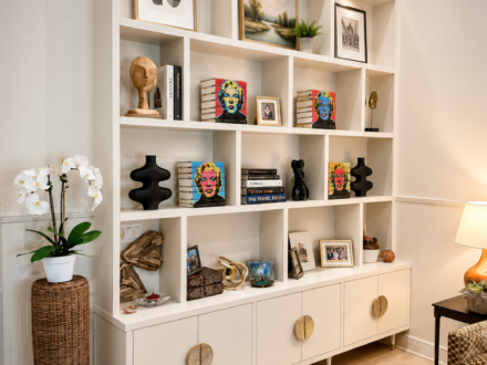 Custom white built-in display cabinet featuring open shelving, decorative storage compartments, lower cabinet storage, styled artwork, books, and decorative accessories in a living room.